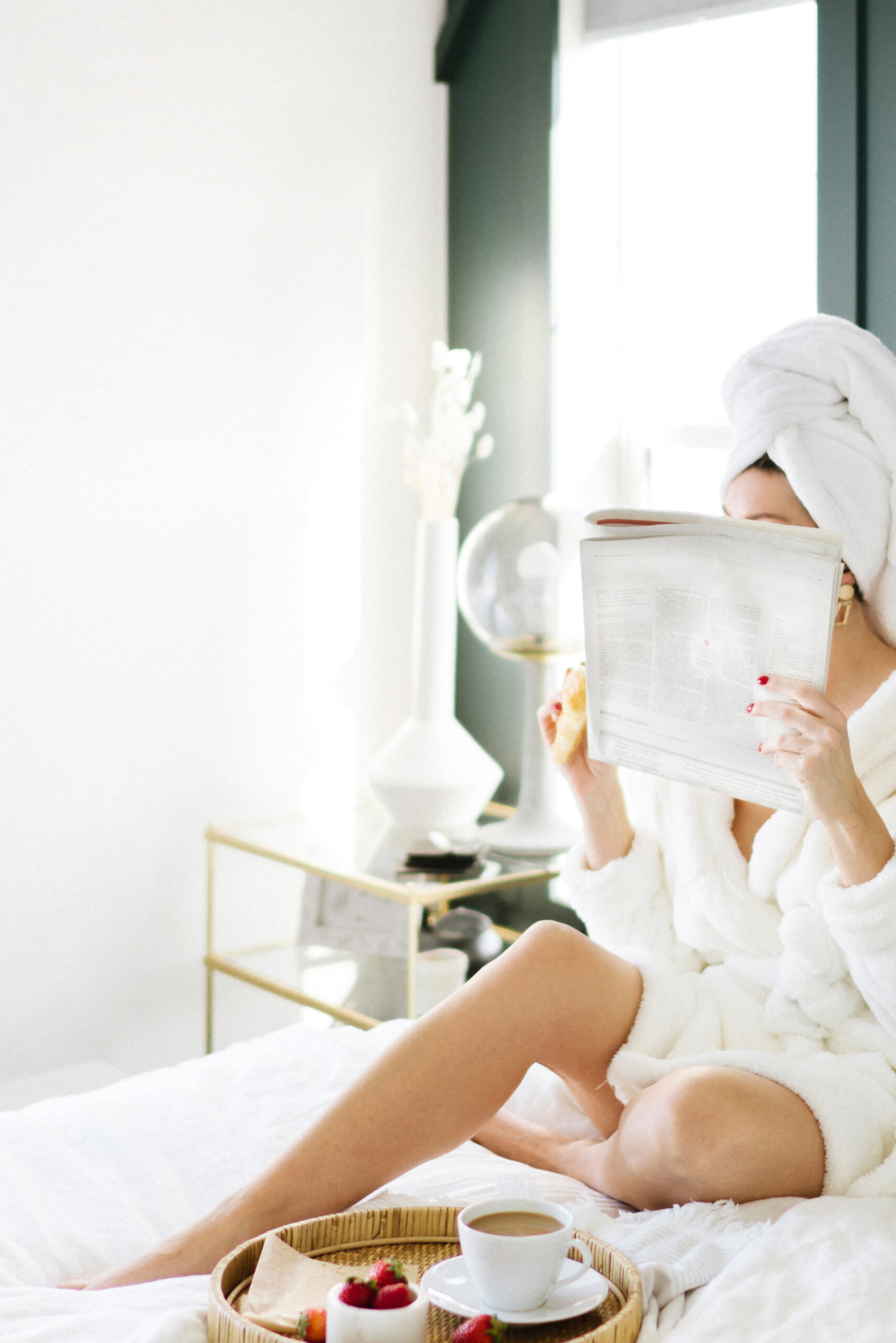 Woman in a bathrobe reading the newspaper on her bed